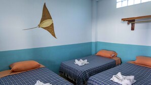 Quarto com duas camas, cada uma com colcha xadrez e almofada laranja. Há uma toalha em cada cama.