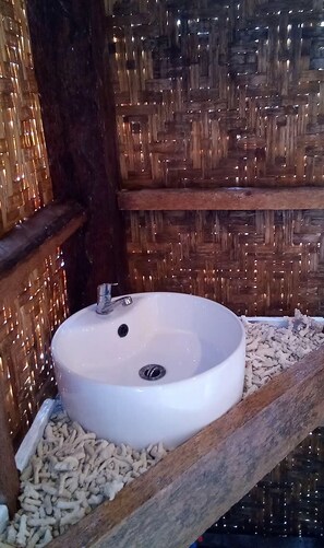 Ein weißes Waschbecken mit Abfluss in einem hölzernen Rahmen vor einer gewobenen Wand.