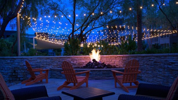 Un espace extérieur aménagé avec des chaises Adirondack et un foyer, entouré de murs en pierre et illuminé de guirlandes lumineuses.