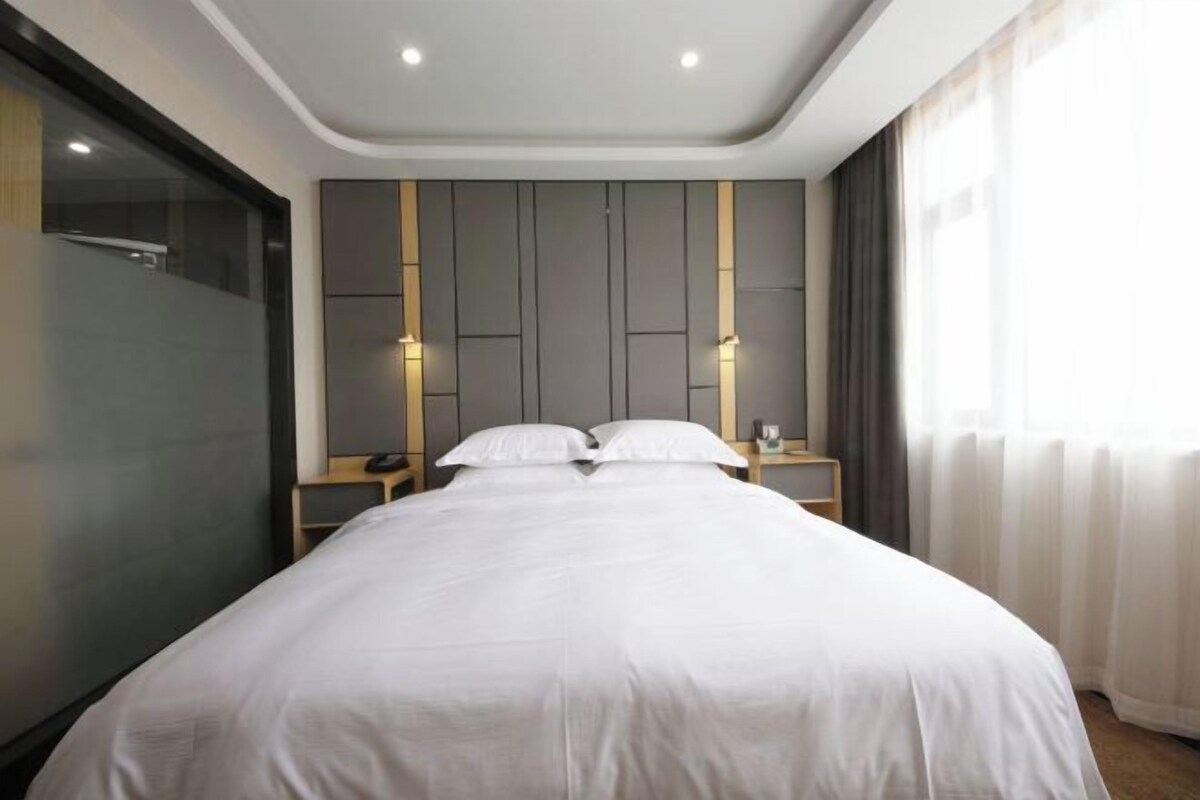 A modern hotel room with a large bed, a bedside table, a nightstand, and a wall-mounted light fixture.