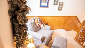 Een gezellige woonkamer met een grijze bank, een klein tafeltje met een lamp en een decoratieve plant.