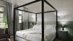 A four-poster bed with white linens, a bedside lamp, and a view of the city through a window with curtains. - Athinaidos Divine Suite by K&K (Αθήνα)