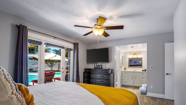 A bedroom with a bed, a ceiling fan, a TV, and a view of the outside. - PHX Scottsdale Oasis 4BR Private Pool Hot Tub Resort-Style Patio Shop Dine Golf (Phoenix)