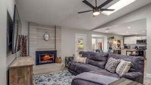 A modern living room with a fireplace, a large sofa, a coffee table, and a ceiling fan. - PHX Scottsdale Oasis 4BR Private Pool Hot Tub Resort-Style Patio Shop Dine Golf (Phoenix)