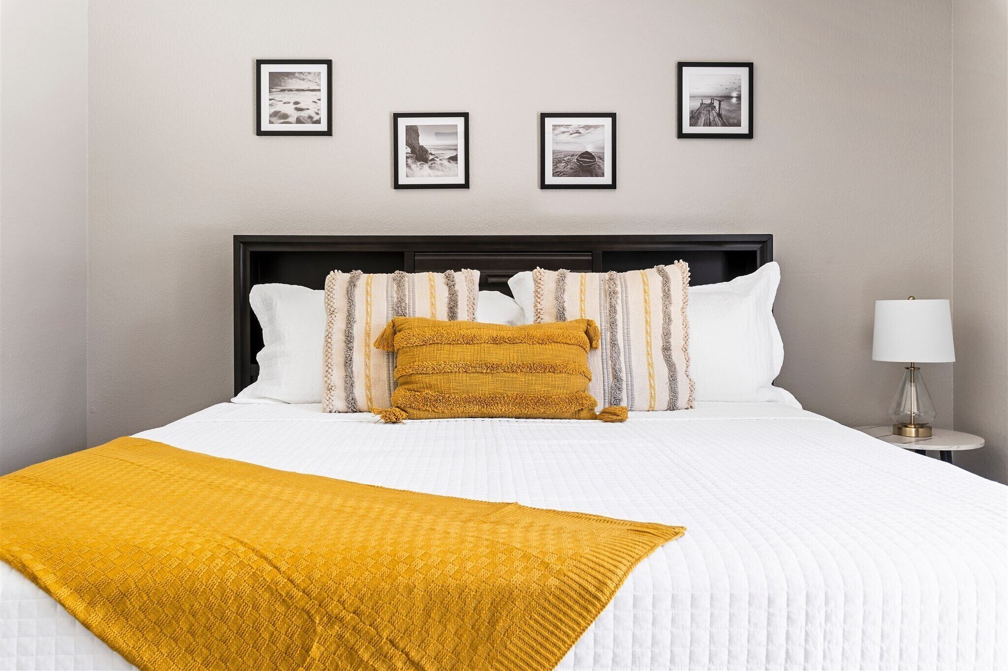A neatly made bed with a white duvet and a mustard-colored throw blanket.
