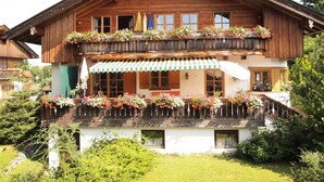 Un chalet en bois à deux étages, doté de balcons ornés de jardinières, d’un auvent à rayures vertes et blanches et d’une façade blanche.