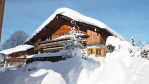 Un chalet en bois avec un toit en pente recouvert de neige, entouré de congères et doté d’un balcon avec des balustrades.