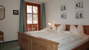 Un lit double avec du linge de lit blanc, une tête de lit en bois, une table de chevet avec une lampe et une fenêtre avec des rideaux.