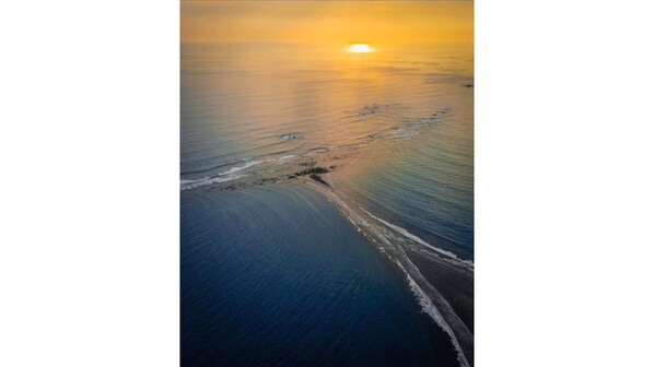 Vue aérienne d’une plage, avec le sillage d’un bateau visible et un coucher de soleil.