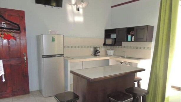 A kitchen with a central island, two stools, a refrigerator, a microwave, and a sink. - Paraíso Chamán 3 (Uvita)
