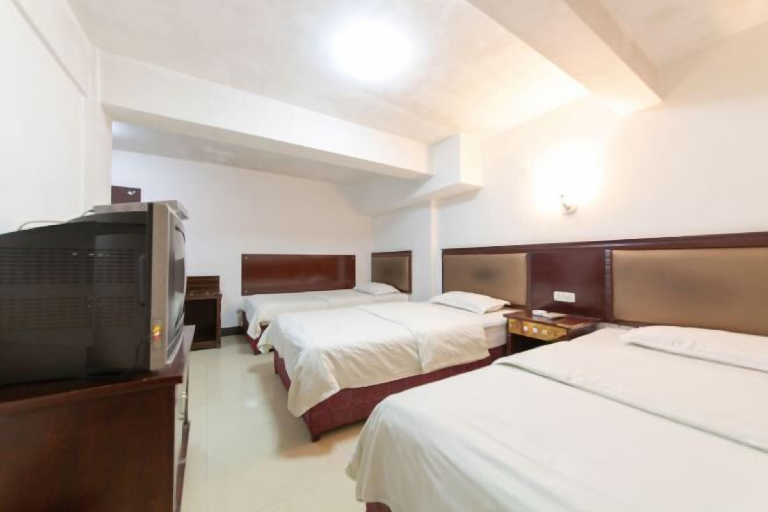 A hotel room with three beds, a television, and a wooden headboard.