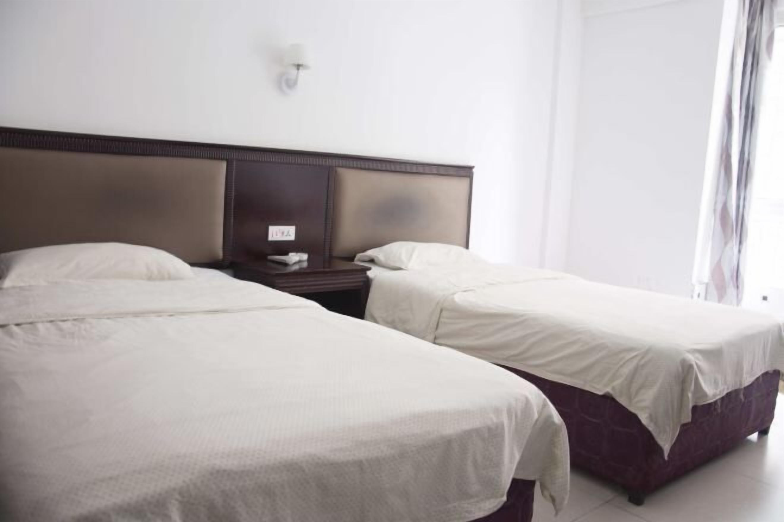 A hotel room with two beds, a nightstand, and a wall-mounted light fixture.