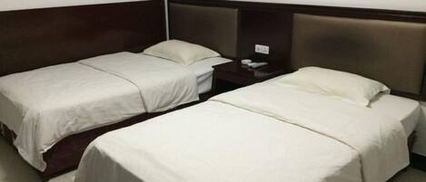 Habitación de hotel con dos camas individuales, una mesita de noche y una lámpara fijada a la pared.