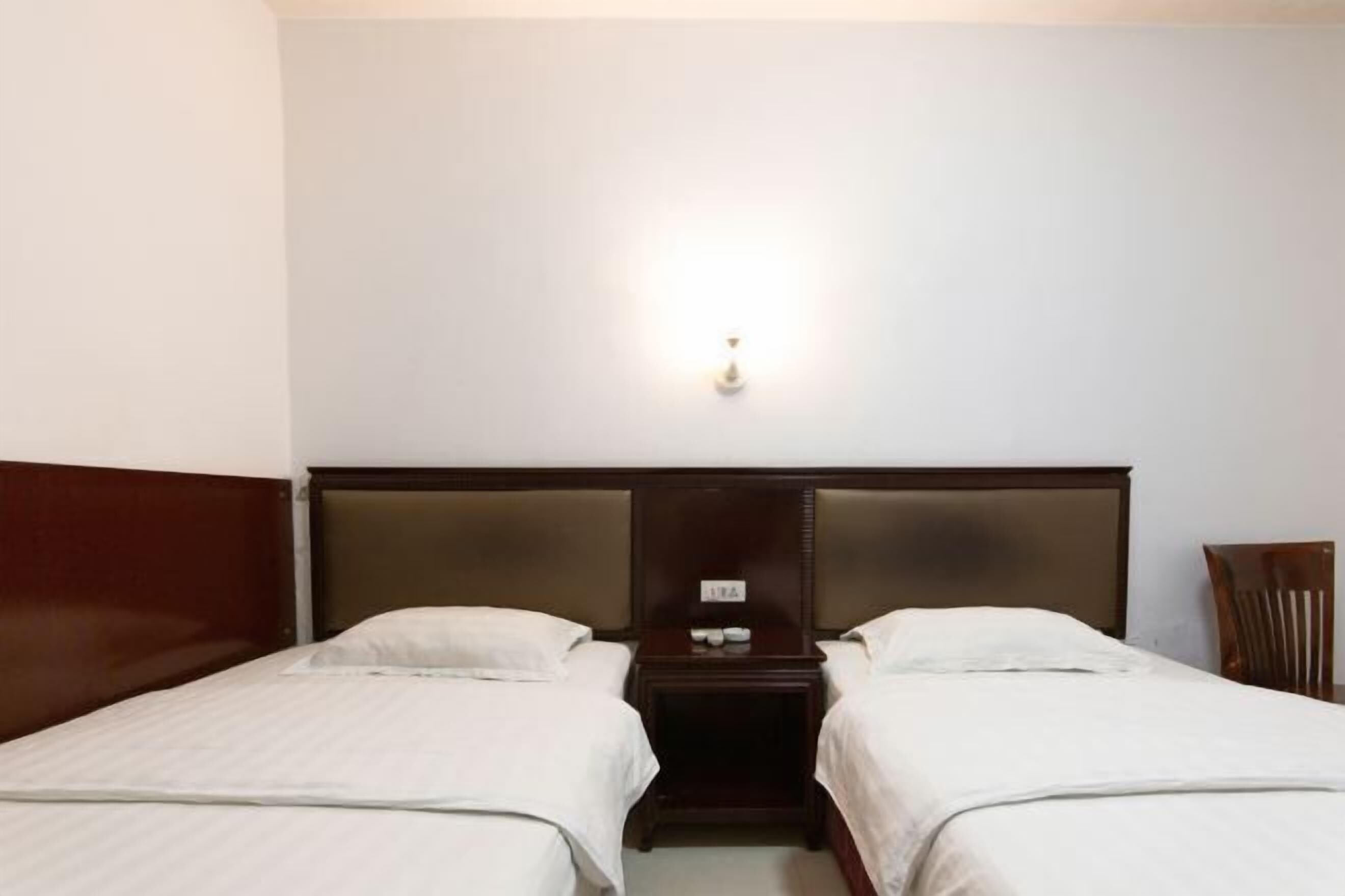Ein Hotelzimmer mit zwei Einzelbetten, einem Holzkopfteil, einem Nachttisch mit Lampe und einem Sessel.