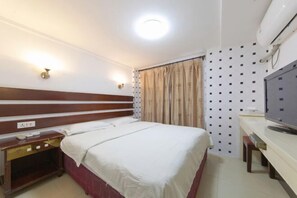 Una habitación de hotel con cama, mesita de noche, televisión y cortinas.