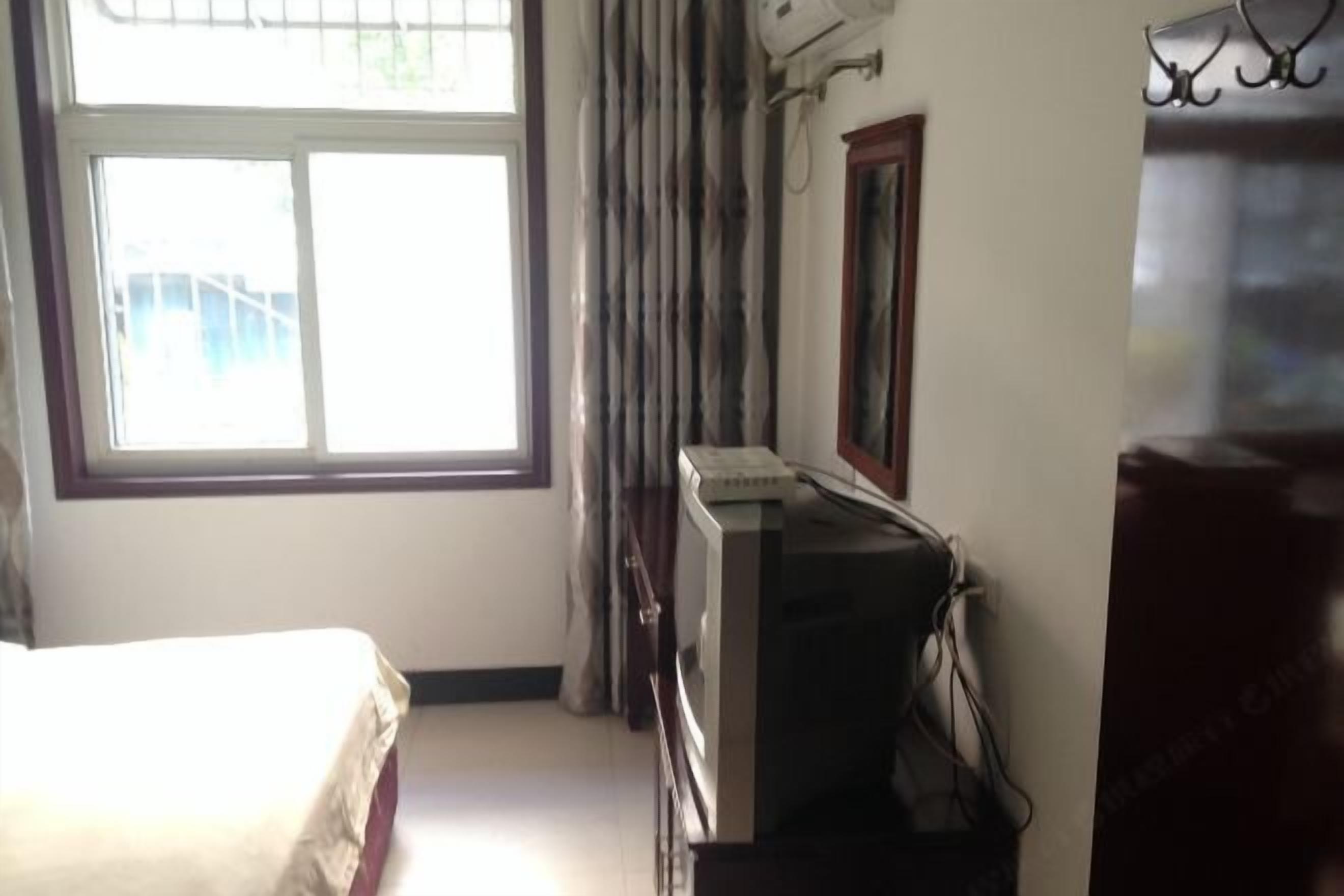 A room with a bed, a television, and a window with curtains.