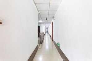 A long, narrow hallway with white walls and a tiled floor, leading to a door at the end. - Caizi Hostel (Huangshi)