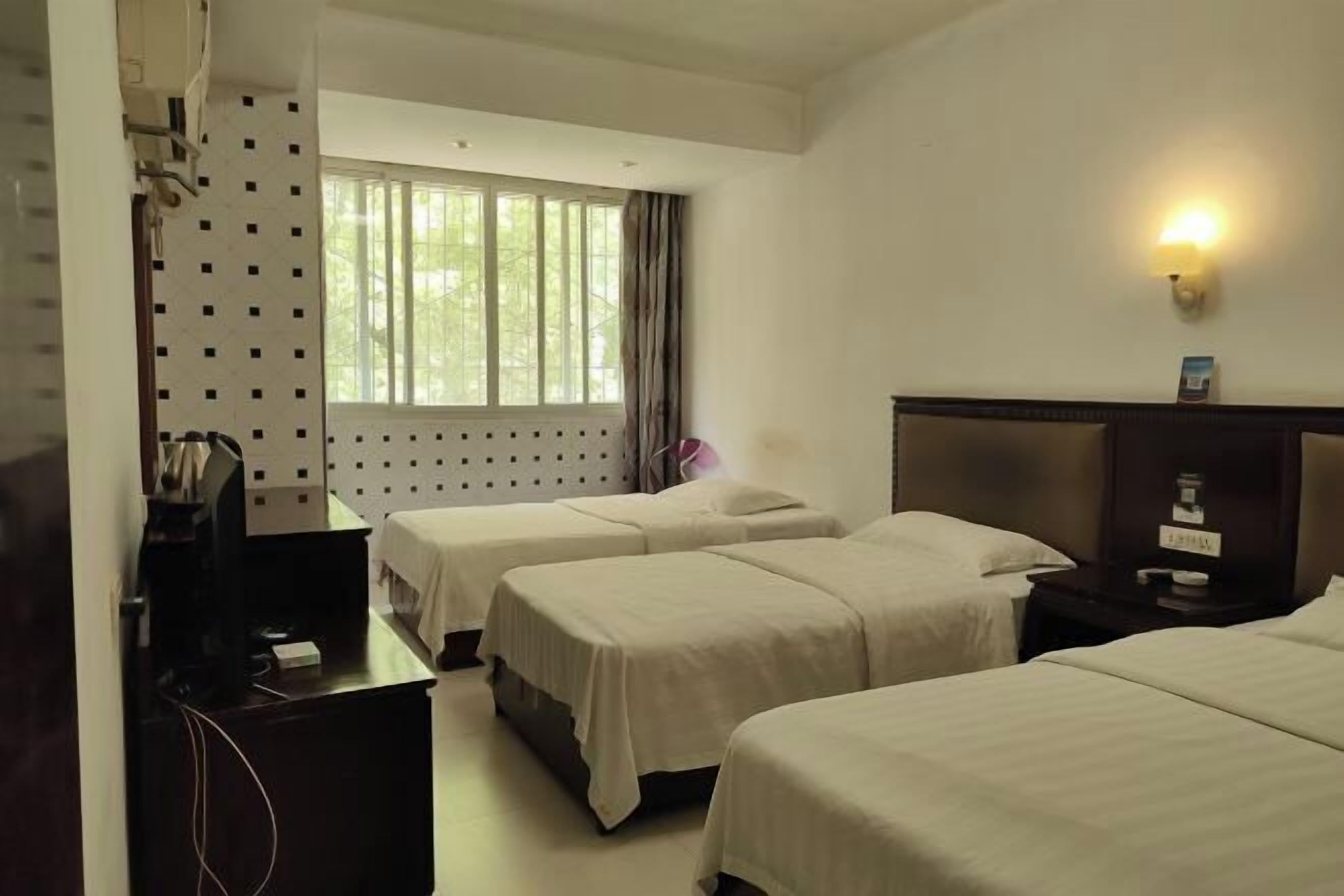 A hotel room with two beds, a desk, a TV, and a window with curtains.