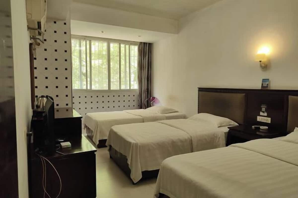 A hotel room with two beds, a desk, a TV, and a window with curtains.