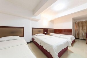 Habitación de hotel con tres camas, cabecera de madera, mesita de noche y ventana con cortinas.