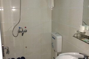 Un baño con ducha, lavamanos, secador de manos y dispensador de papel higiénico.