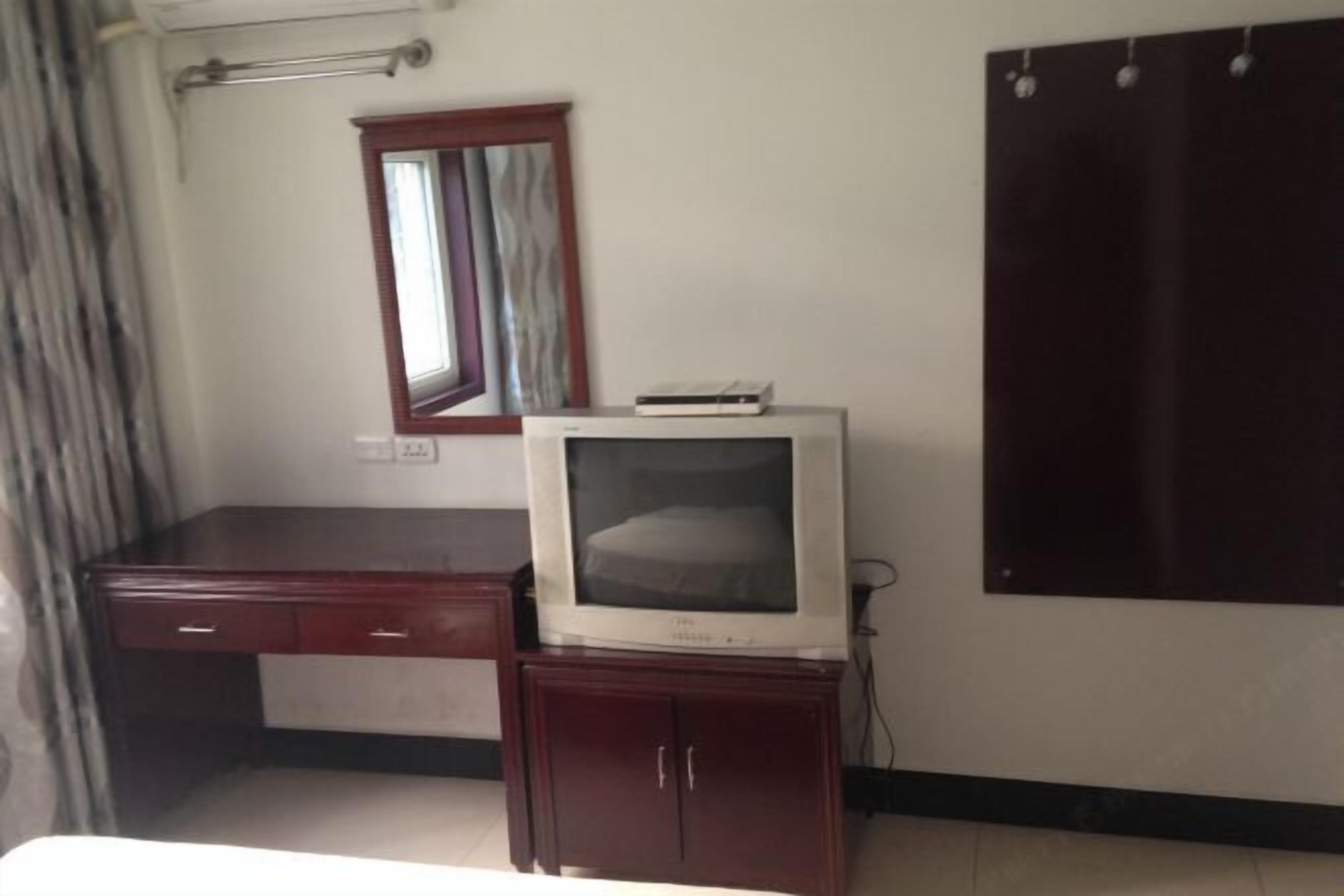 A room with a wooden desk, a television on a cabinet, a mirror, and a wardrobe.