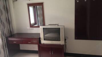 A room with a wooden desk, a television on a cabinet, a mirror, and a wardrobe.