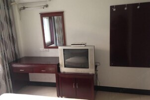 Una habitación con un escritorio de madera, un televisor en un mueble, un espejo y un armario.