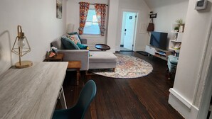 Ein gemütliches Wohnzimmer mit Essbereich, Holzboden, einem Fernseher und einem kleinen Teppich.