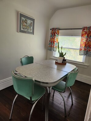 A dining area with a table and four chairs, a potted plant on the table, a window with floral curtains, and a framed picture on the wall. - Beautiful 120 year old home in downtown Kansas City. (Kansas City)