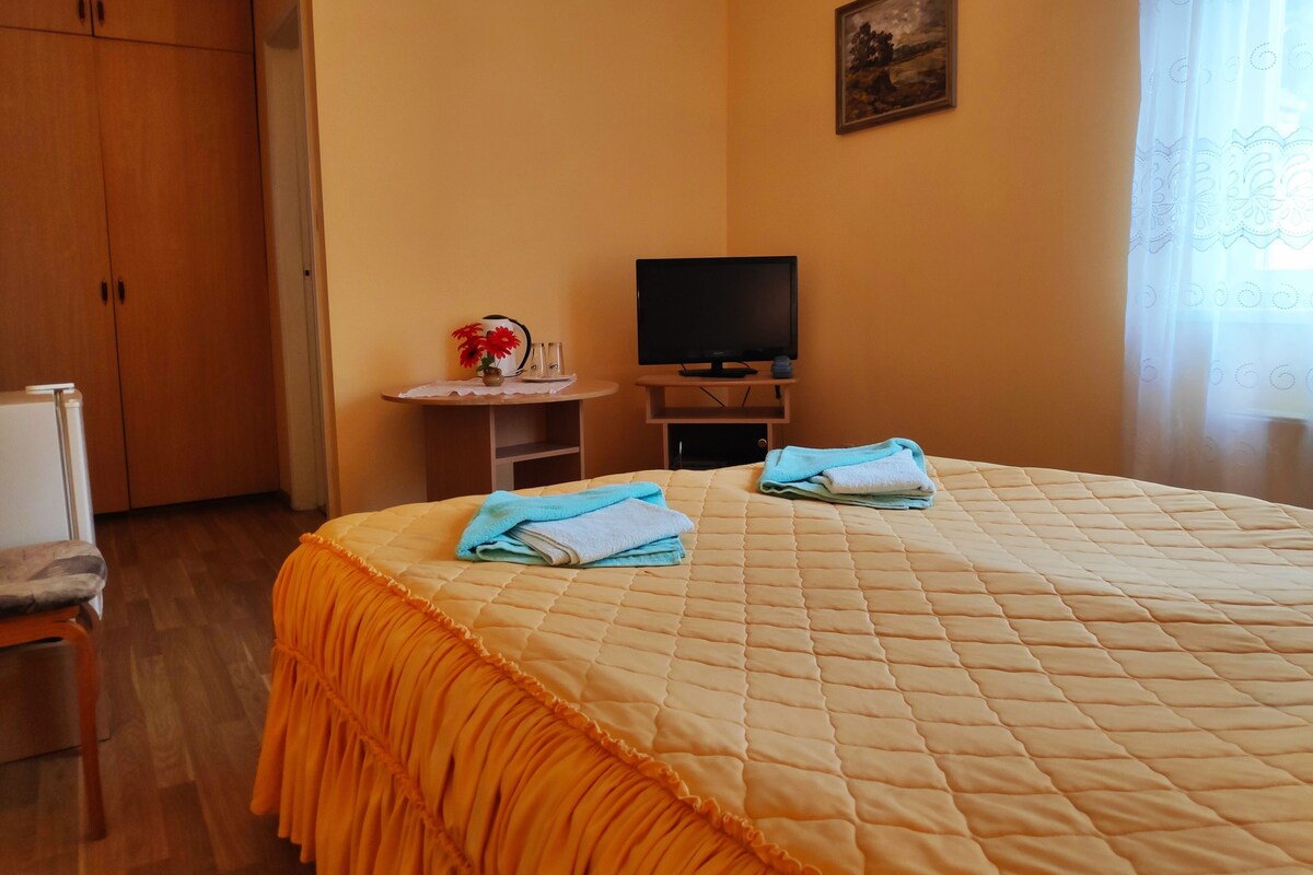 A hotel room with a bed, a television, a small table with a vase of flowers, and a wardrobe.