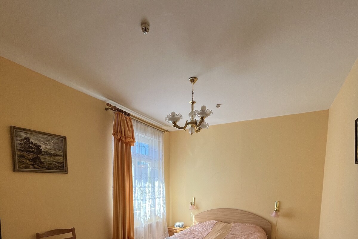 A bedroom with a bed, a desk, a chair, a dining table, and a small table with a lamp.