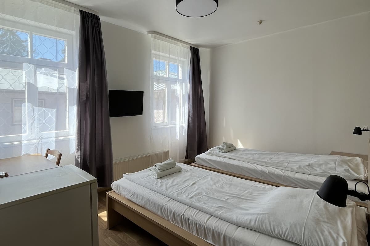 A hotel room with two beds, a desk, a chair, and a window with curtains.