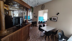 A bar area with a wooden counter, a television, and a plant. There is a dining area with a table and chairs. - Hotel Elīna (Jurmala)