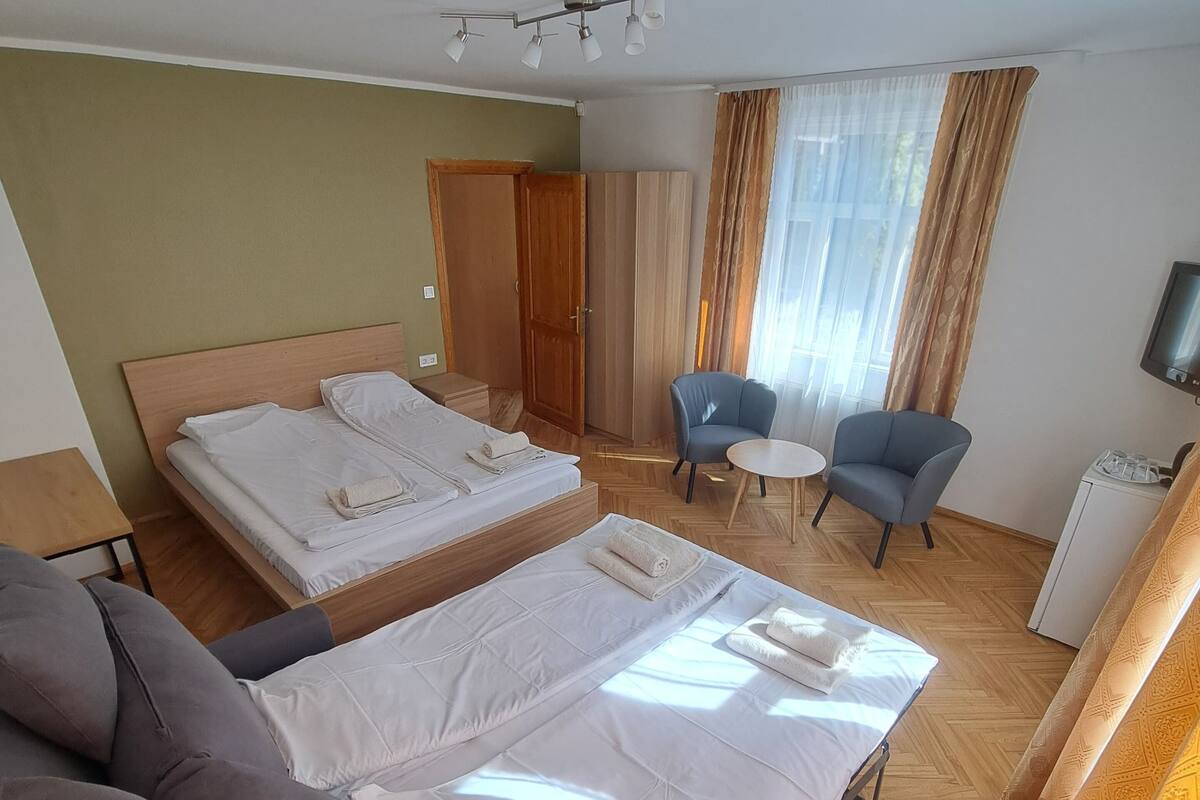 A hotel room with two beds, a sofa, a chair, a TV, and a wardrobe.