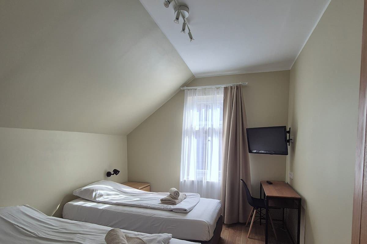A hotel room with two beds, a desk, a TV, and a window with curtains.