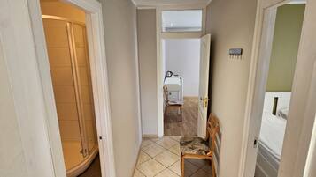 Un pasillo con suelo de baldosas, una silla de madera y una puerta que da a un baño.