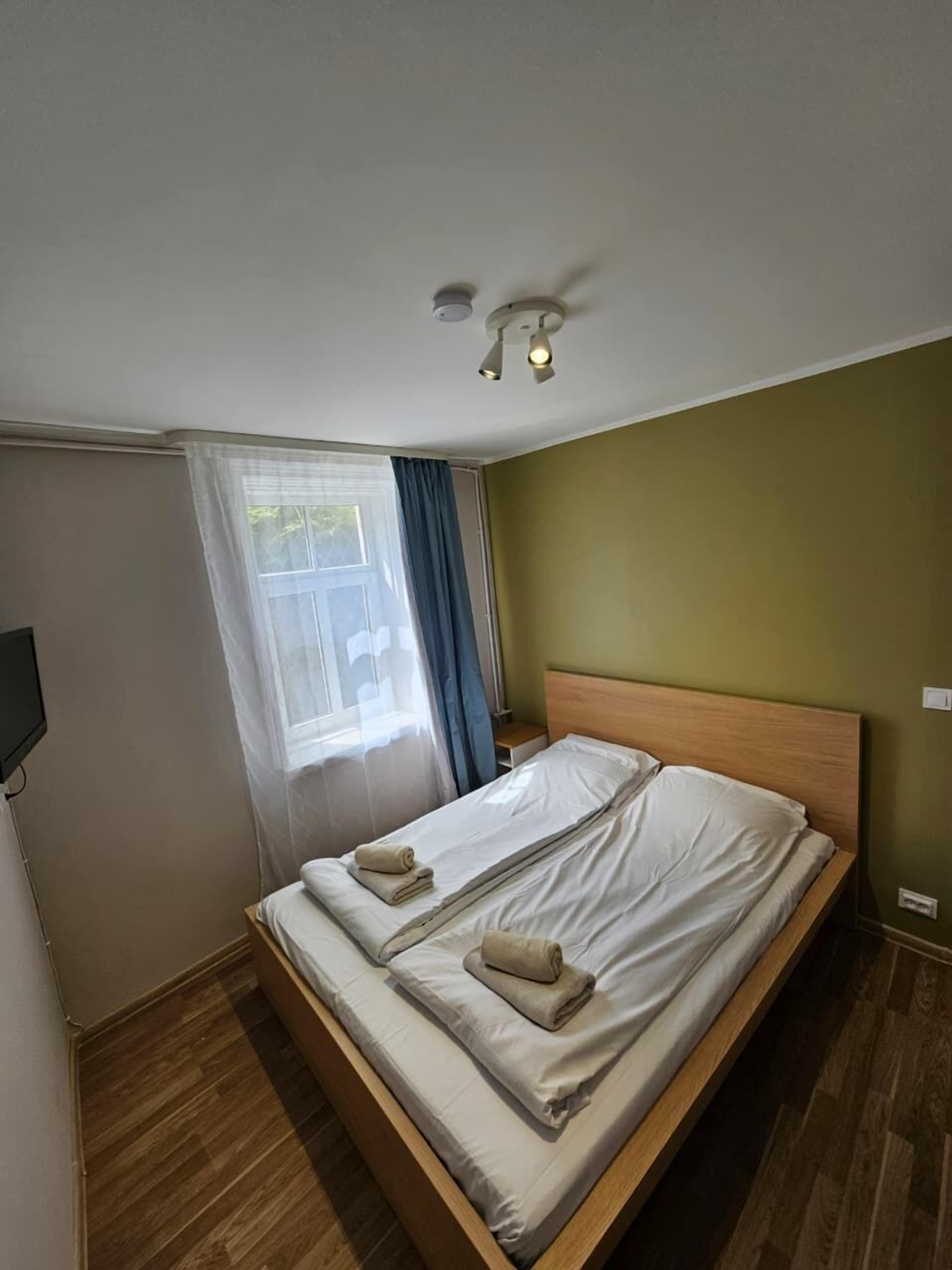 Een enkel bed met een houten hoofdbord, een plafondventilator en een raam met gordijnen.