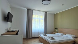 A hotel room with a bed, a desk with a computer, a TV, and a window with curtains. - Hotel Elīna (Jurmala)