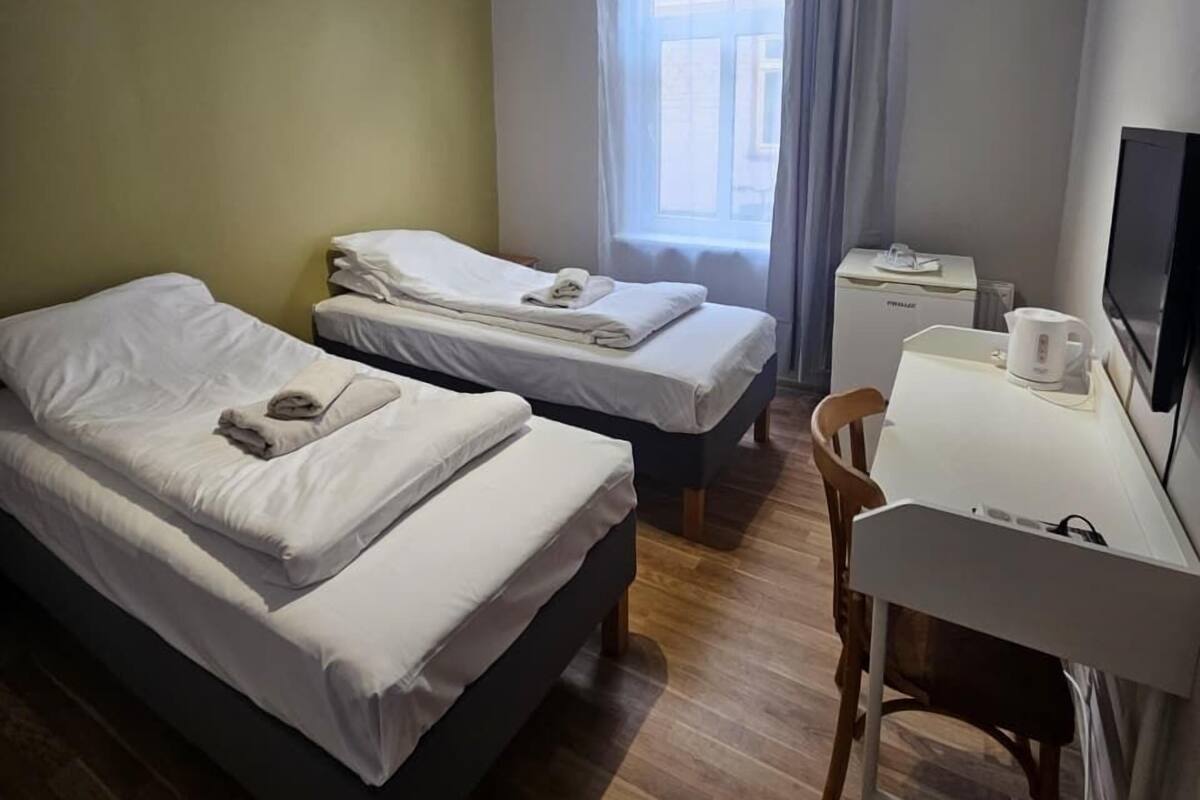 A hotel room with two beds, a desk, a chair, a TV, and a window with curtains.