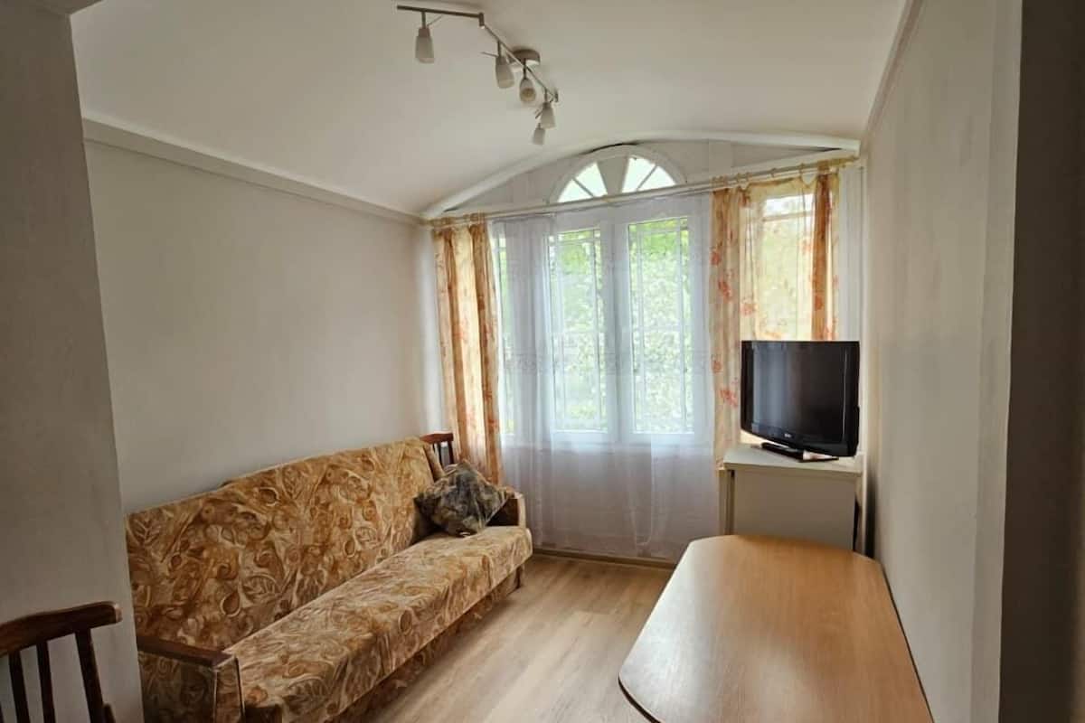 A room with a sofa, a wooden table, a TV, and a window with curtains.