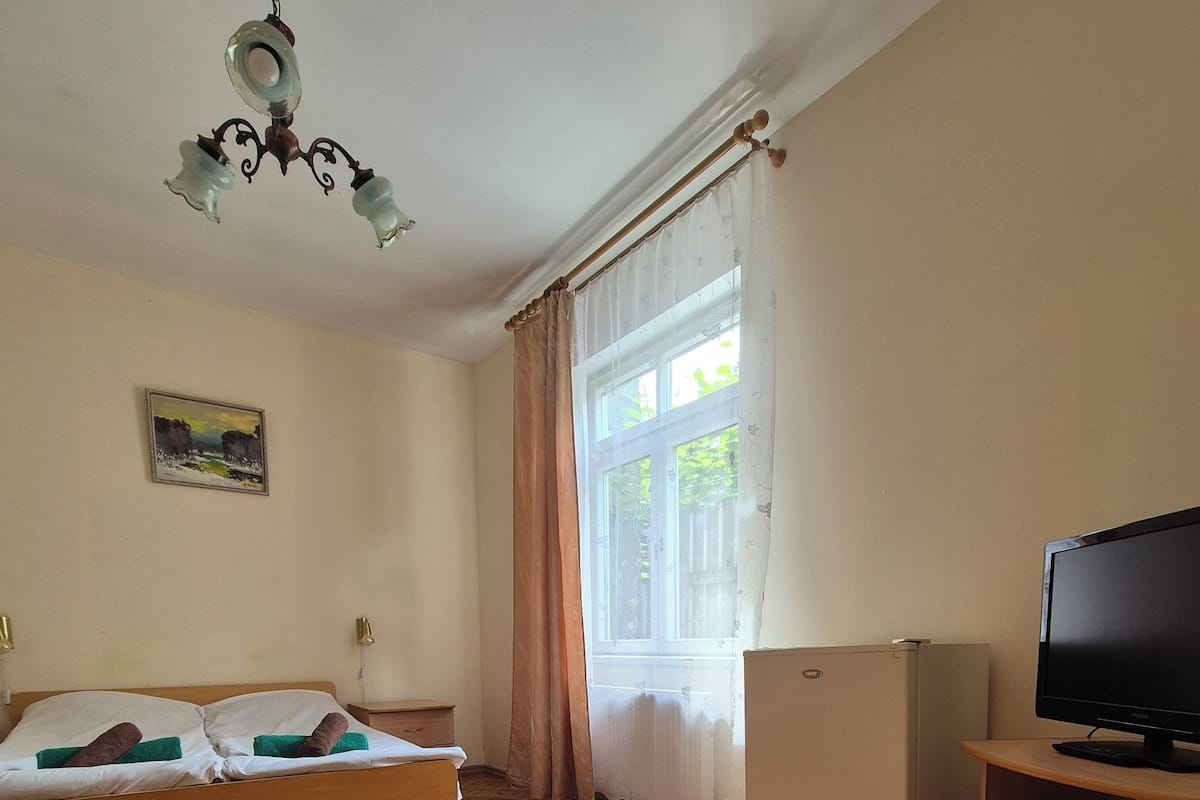 A room with a bed, a television, a window with curtains, and a patterned floor.