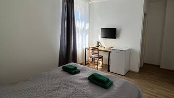 A hotel room with a bed, a desk, a chair, a television, and a door.