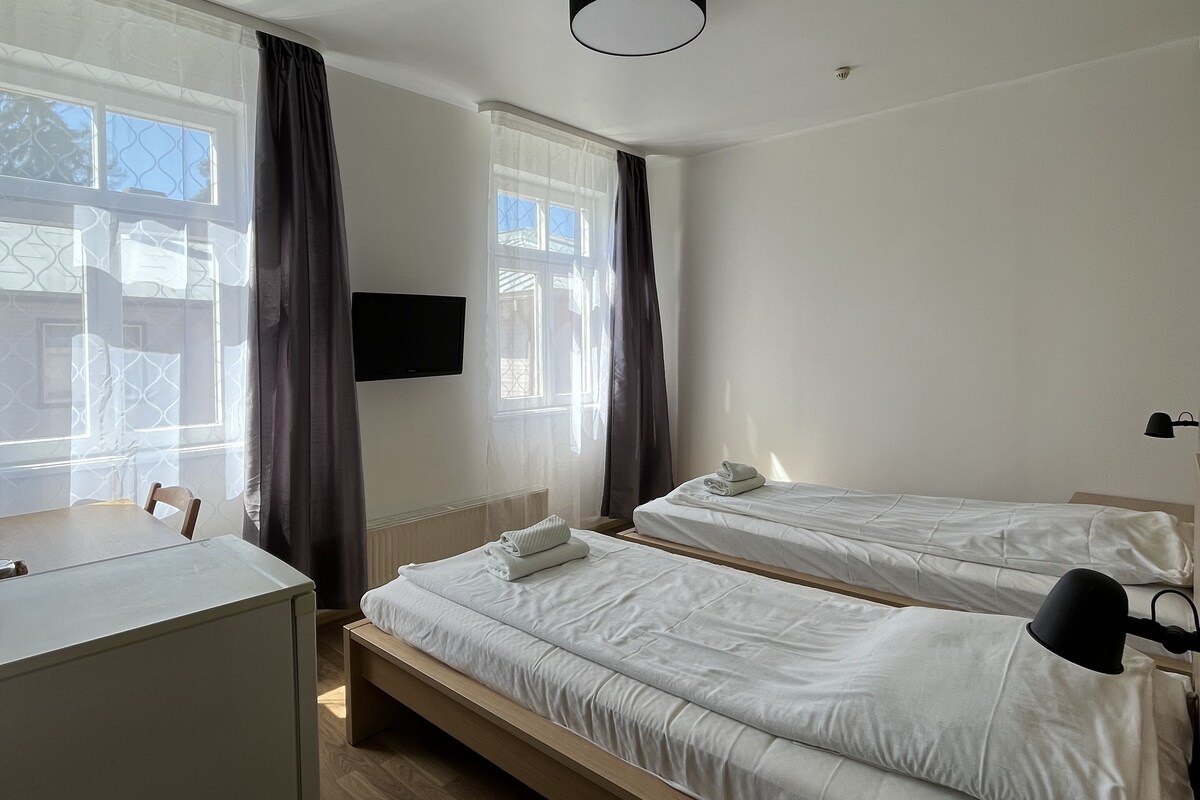 A hotel room with two beds, a desk, a chair, a TV, and a window with curtains.
