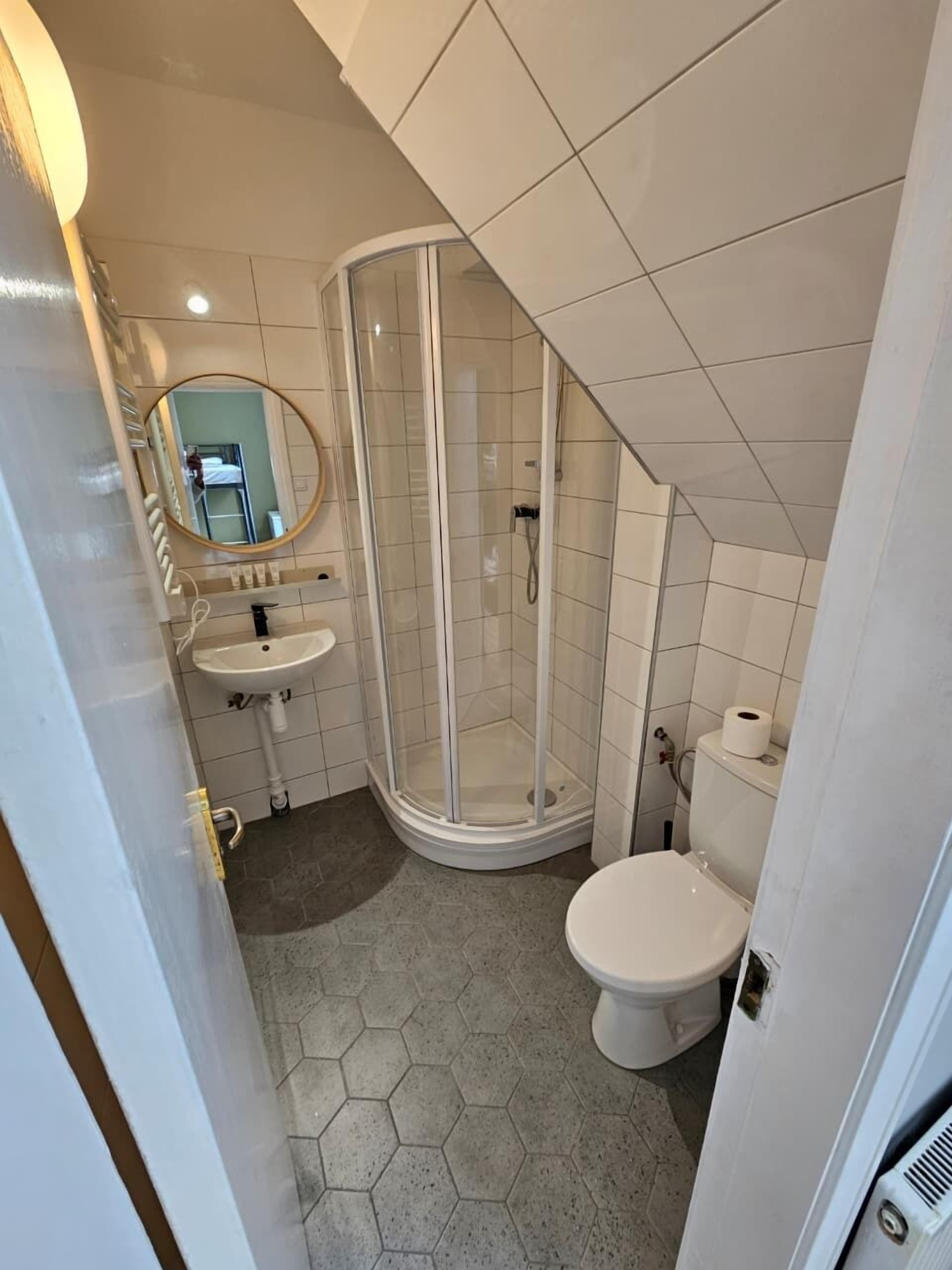 A bathroom with a shower, toilet, sink, and a mirror.