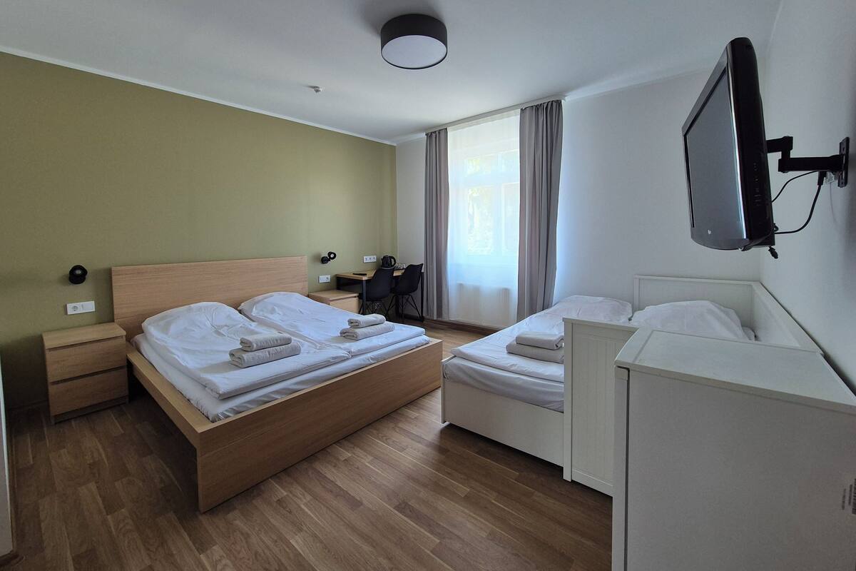 A hotel room with two beds, a desk, a chair, a TV, and a wardrobe.
