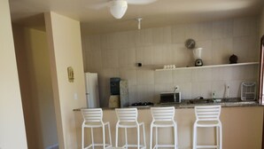 Ein Essbereich mit einem weißen Tisch und Stühlen, ein Küchenbereich mit Mikrowelle und Herd sowie ein Deckenventilator.