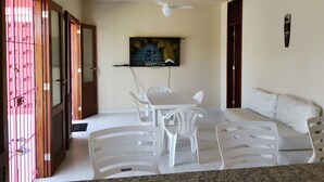 Ein Zimmer mit Esstisch, Stühlen, Deckenventilator, Wandfernseher und einer Couch.