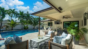 Un espace extérieur aménagé avec des meubles en osier, une piscine et des palmiers, le tout abrité.
