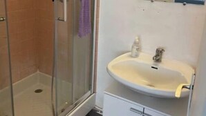 Een badkamer met een douchecabine van glas, een wastafel met een spiegel erboven en een kastje eronder.